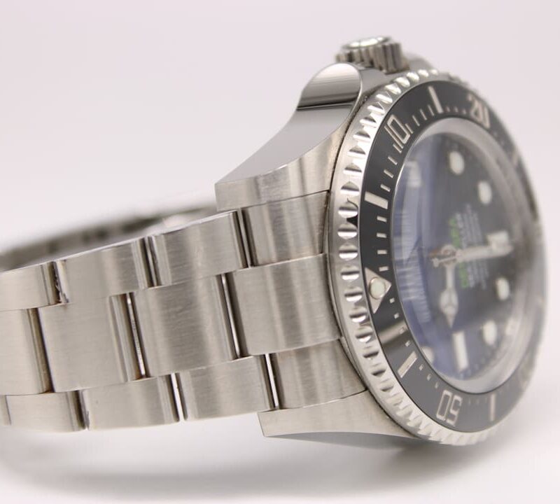 Close-up of a stainless steel diving watch with a black bezel and blue dial on a white background